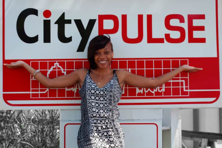 Michelai Graham smiling as she stands outside in front of the City Pulse sign.